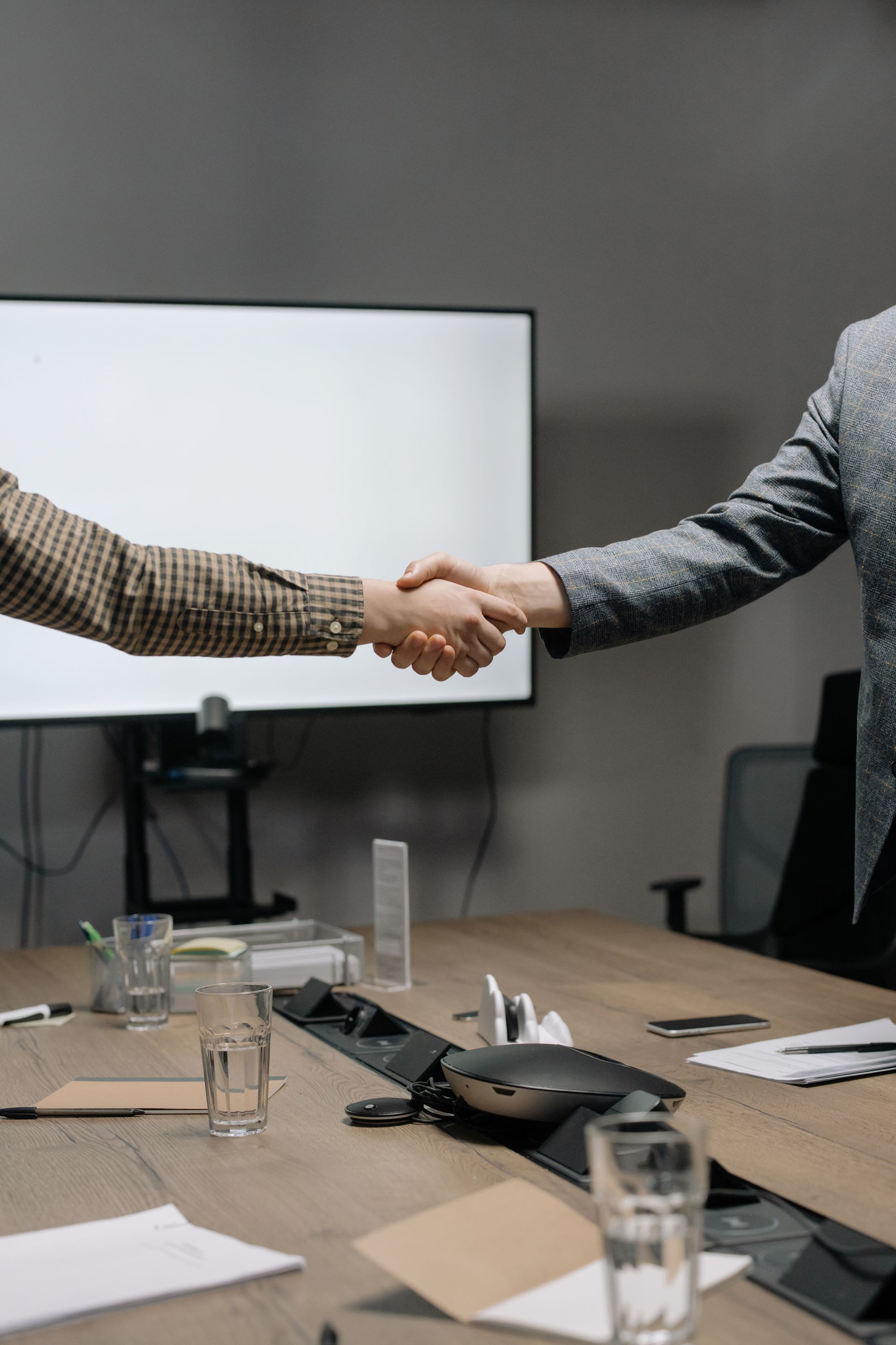 Two people shaking hands across a meeting room table