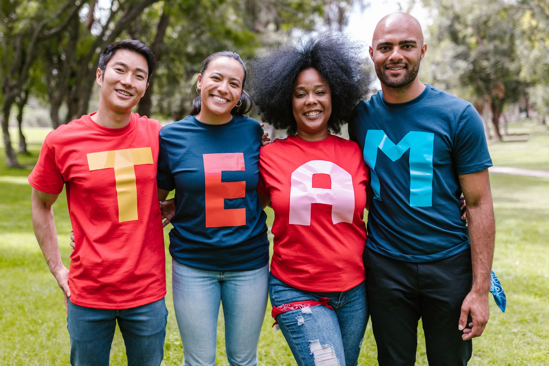 Four smiling friends in a park wearing T-E-A-M letter shirts