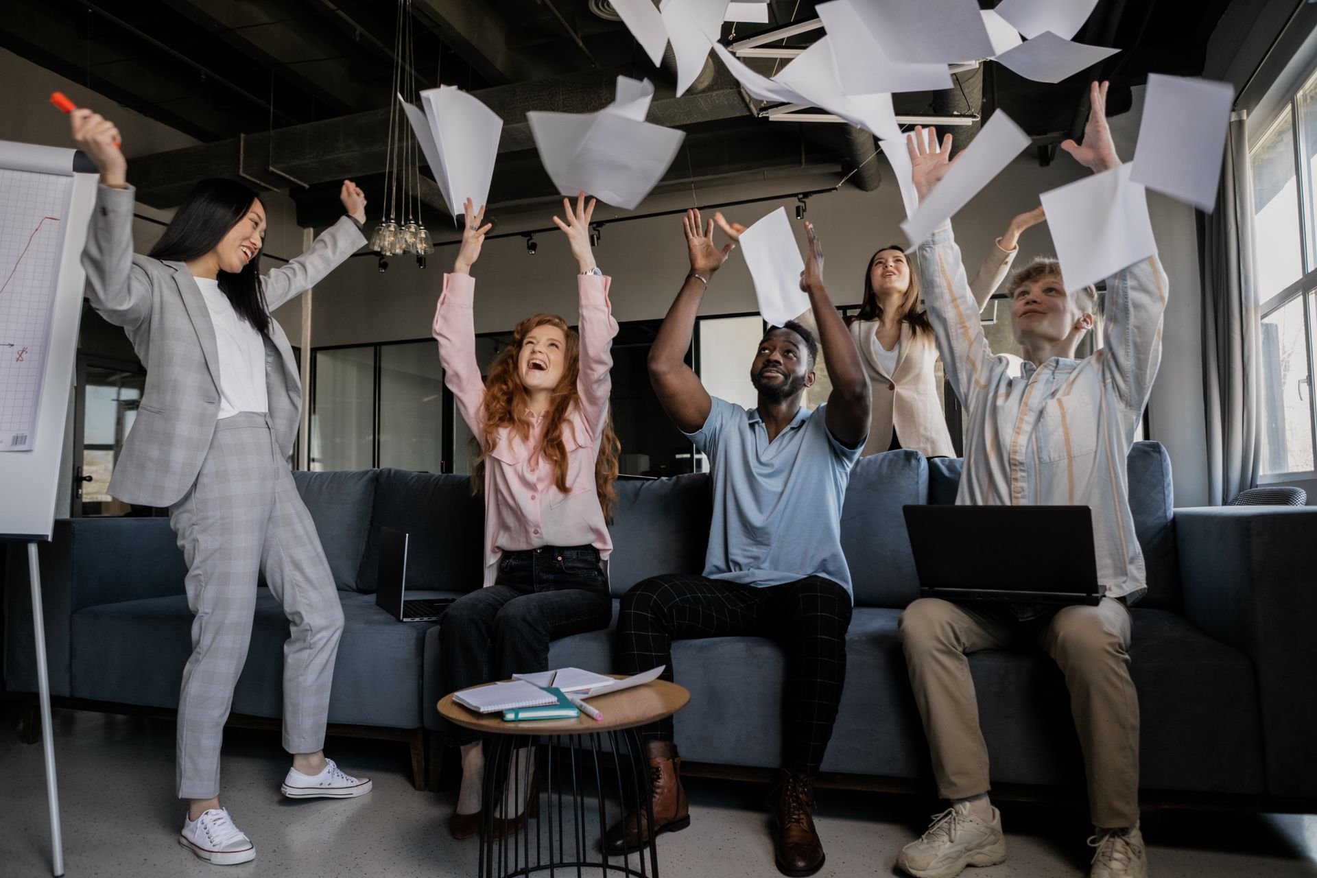 A team in a loft office tossing papers into the air in celebration
