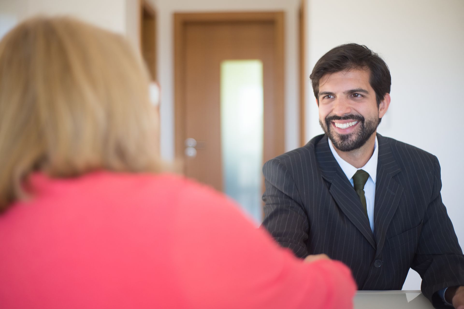 A smiling man in a pinstriped suit greeting a client whose back is to the camera