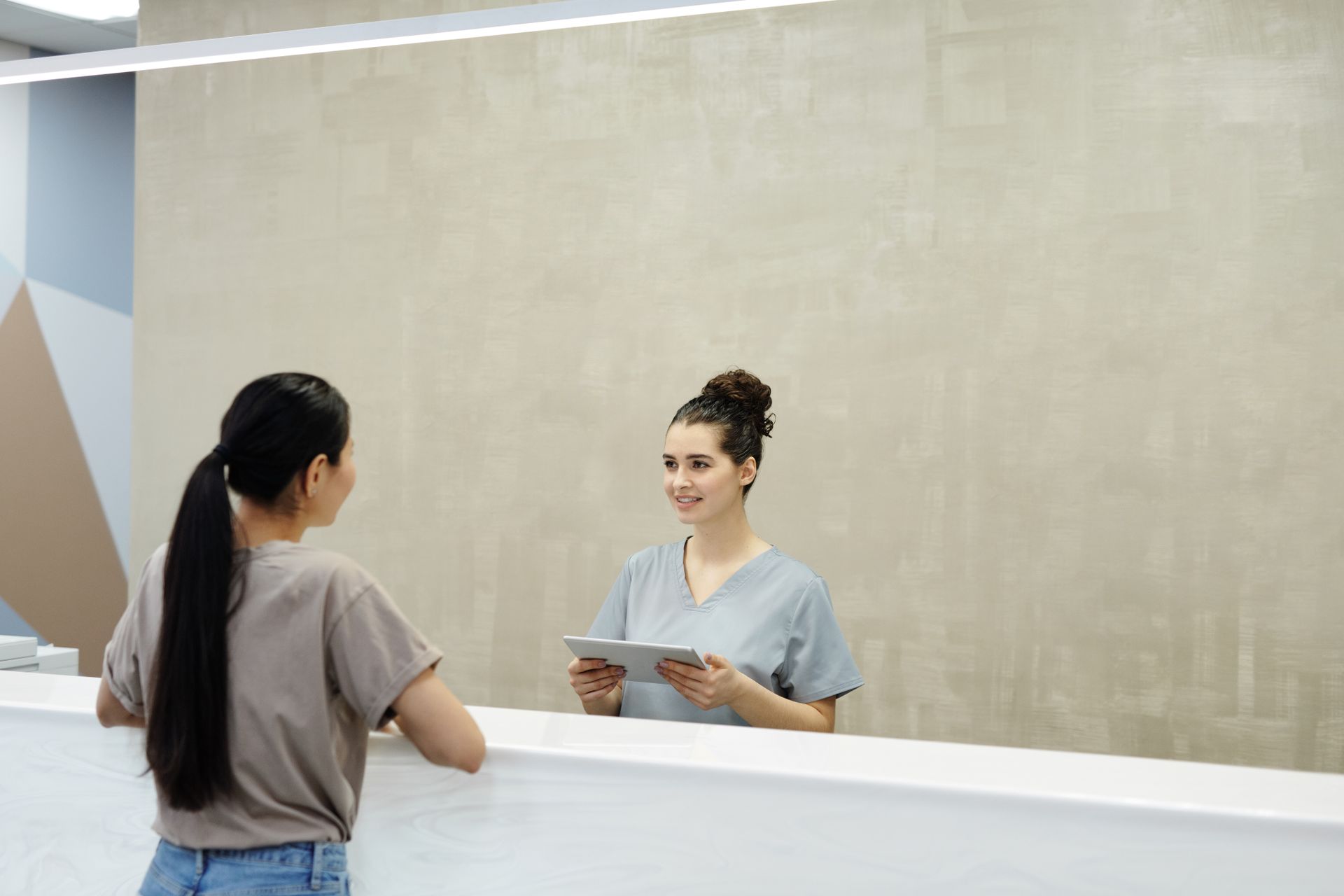 A smiling receptionist holding a tablet, greeting a visitor at a clinic reception desk