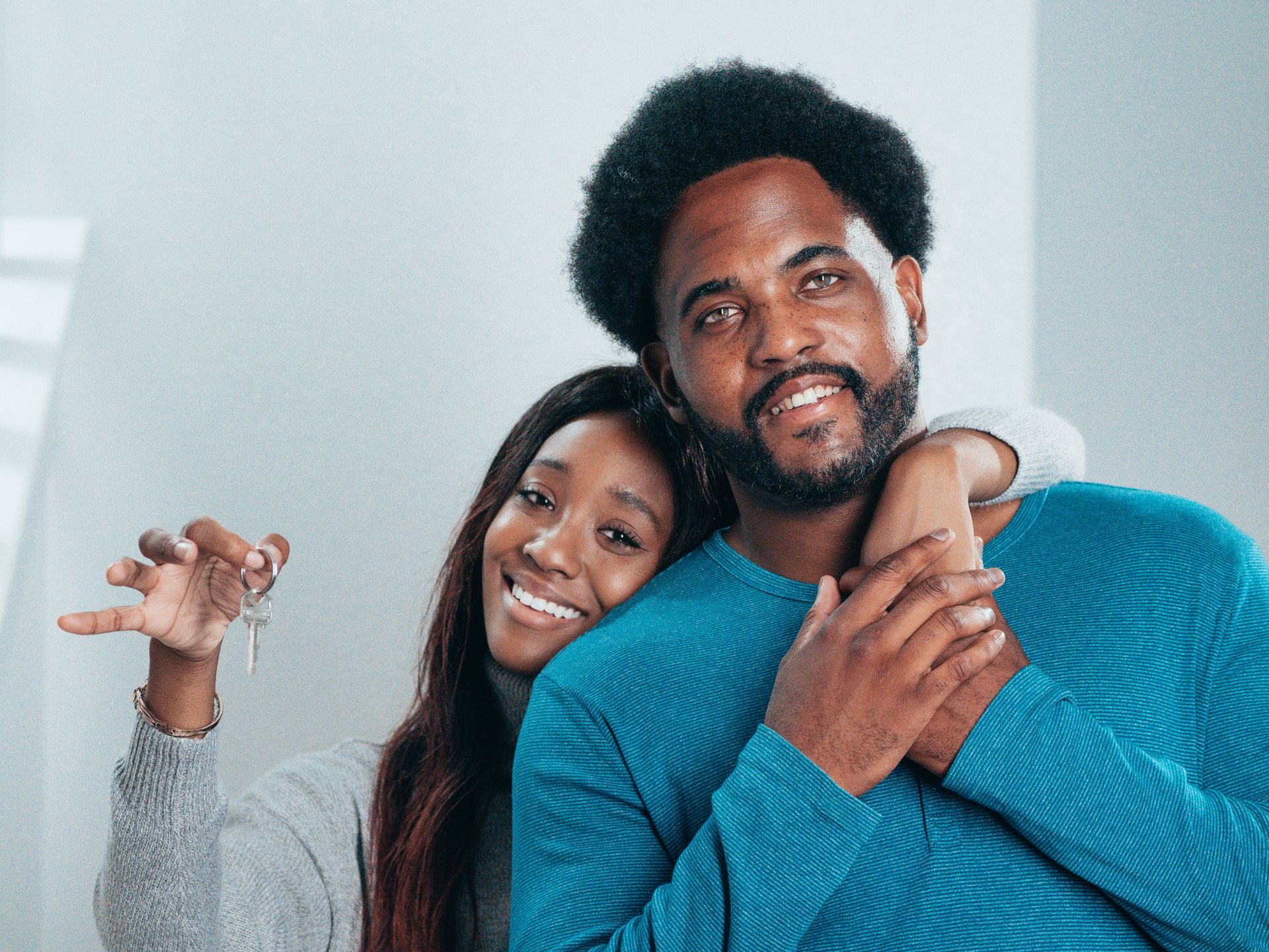 A smiling couple hugging, one holding up a set of keys