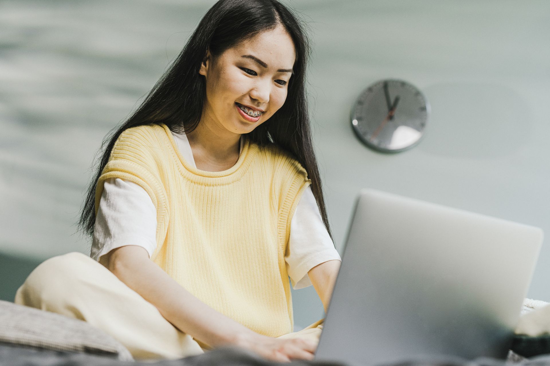 A smiling woman in a white shirt looking down at a laptop she holds, with design drawings on the desk behind her